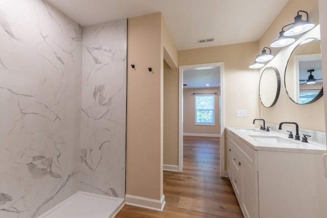 bathroom with a tile shower, hardwood / wood-style flooring, vanity, and ceiling fan