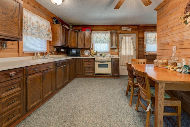 kitchen with a textured ceiling, light carpet, wooden walls, and white stove