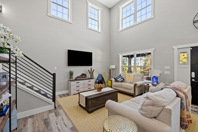 living room with light wood-type flooring, a towering ceiling, and a healthy amount of sunlight