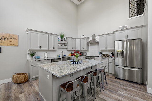 kitchen with light stone counters, a kitchen island, wall chimney exhaust hood, stainless steel appliances, and light hardwood / wood-style floors