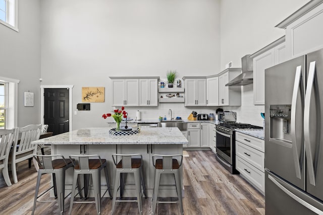 kitchen with dark wood-type flooring, appliances with stainless steel finishes, light stone counters, and a center island