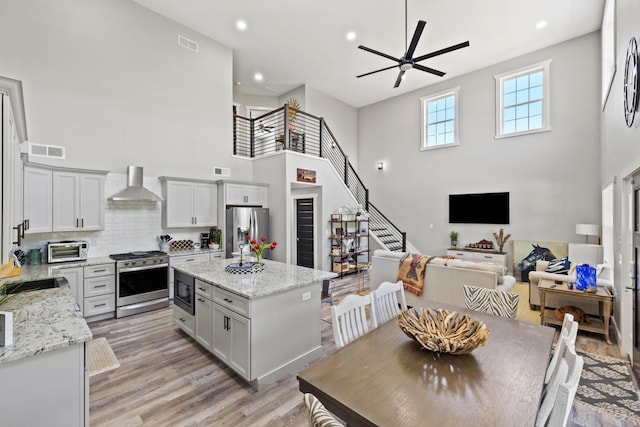 kitchen featuring a kitchen island, light stone counters, stainless steel appliances, light hardwood / wood-style floors, and a high ceiling