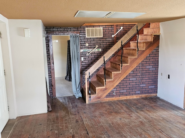 interior space featuring brick wall, a textured ceiling, and hardwood / wood-style floors