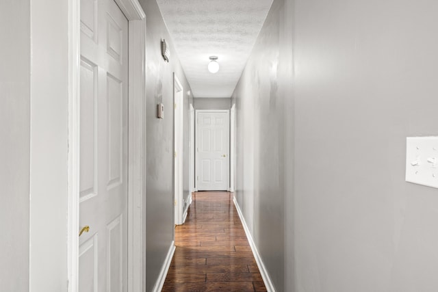 corridor with a textured ceiling and dark hardwood / wood-style flooring