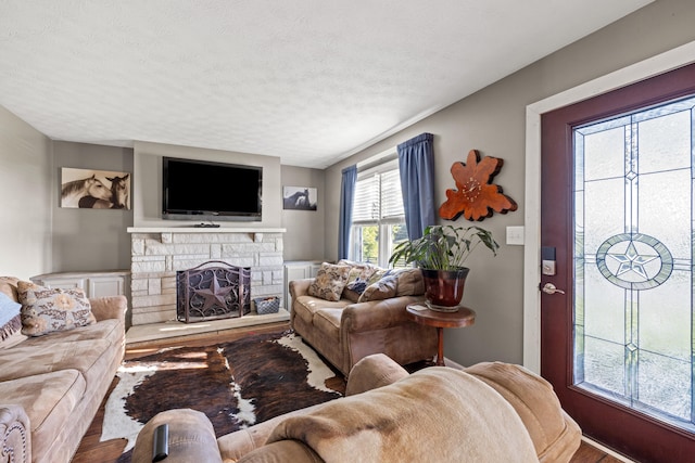 living room featuring a stone fireplace, hardwood / wood-style floors, and a textured ceiling