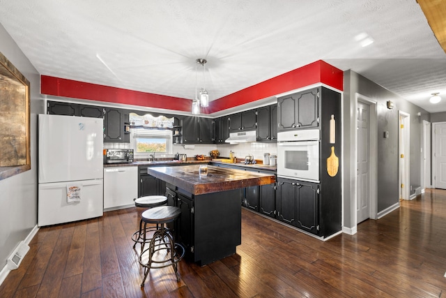 kitchen with appliances with stainless steel finishes, a textured ceiling, a center island, dark wood-type flooring, and a breakfast bar area