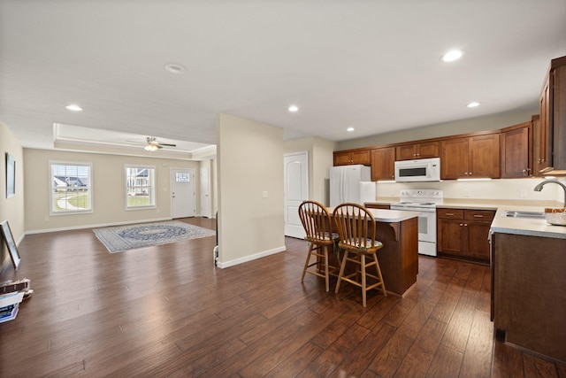 kitchen featuring sink, dark hardwood / wood-style floors, a breakfast bar area, white appliances, and a center island