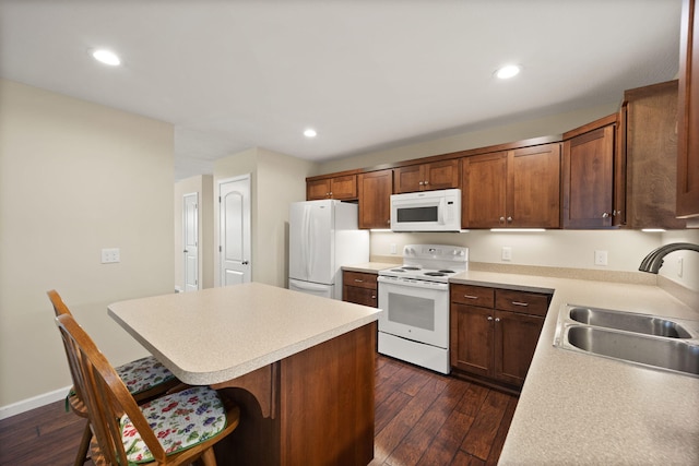 kitchen featuring dark hardwood / wood-style flooring, sink, a kitchen island, a breakfast bar, and white appliances