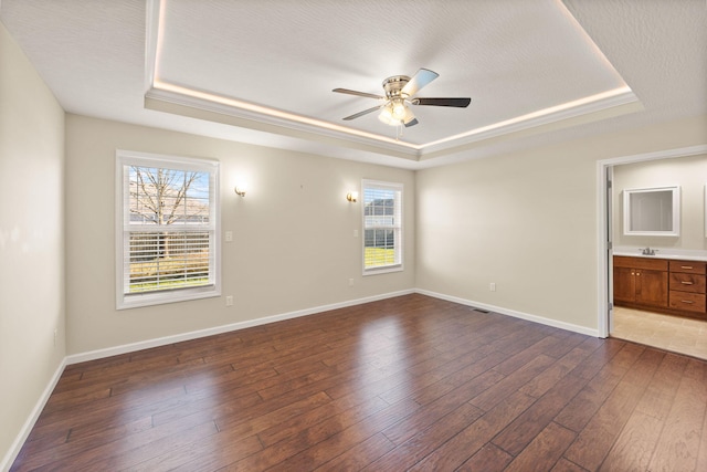 spare room with dark wood-type flooring, ceiling fan, and a raised ceiling