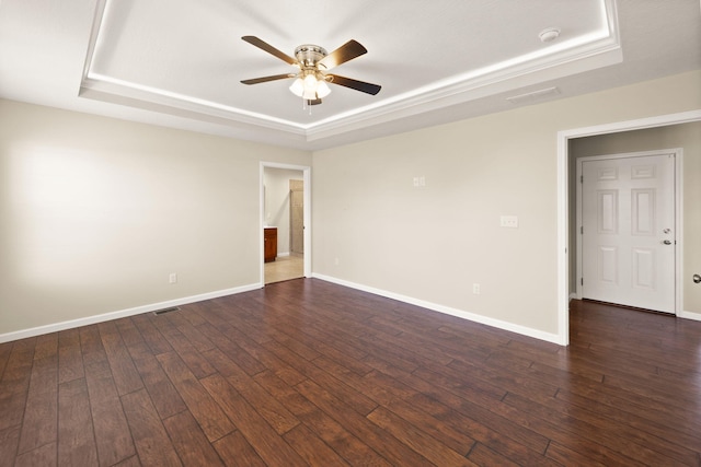 empty room featuring ceiling fan, a tray ceiling, and dark hardwood / wood-style floors