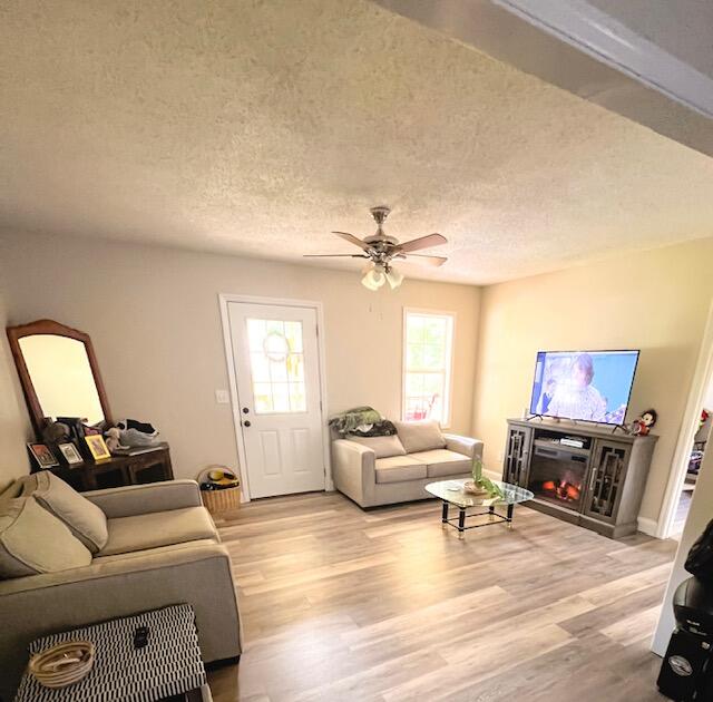 living room with ceiling fan, a textured ceiling, and light hardwood / wood-style floors