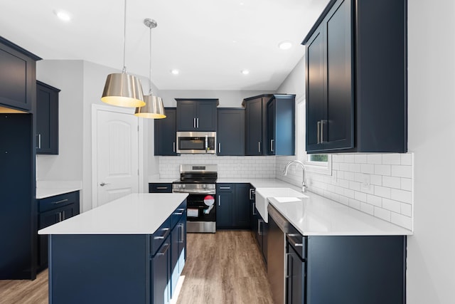 kitchen featuring tasteful backsplash, a kitchen island, appliances with stainless steel finishes, light wood-type flooring, and a sink