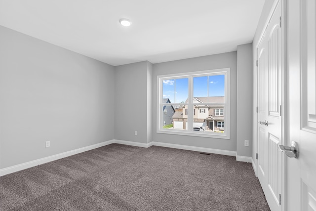 empty room featuring baseboards, visible vents, and dark carpet