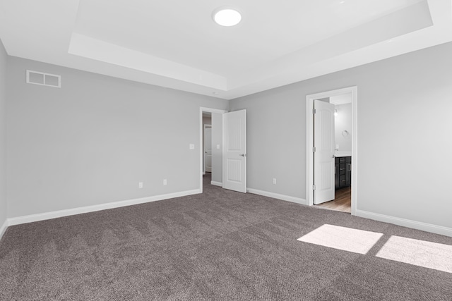 unfurnished bedroom with a tray ceiling, visible vents, ensuite bathroom, carpet flooring, and baseboards