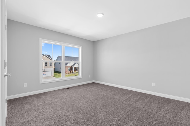 empty room with dark colored carpet, visible vents, and baseboards