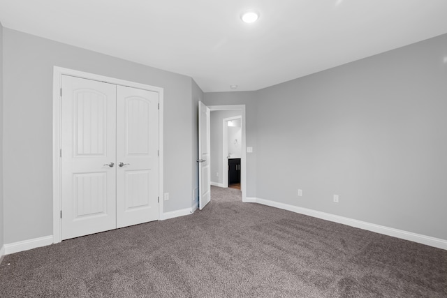 unfurnished bedroom featuring baseboards, dark colored carpet, and a closet