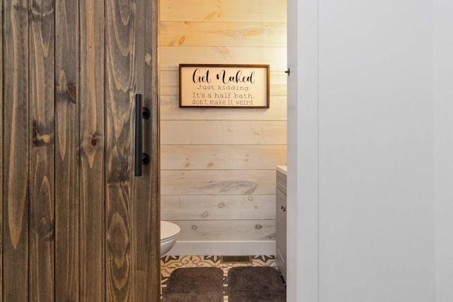 bathroom featuring tile patterned floors, vanity, wooden walls, and toilet