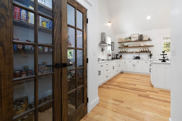 bar with white cabinets, lofted ceiling, wall chimney exhaust hood, gas cooktop, and light hardwood / wood-style floors