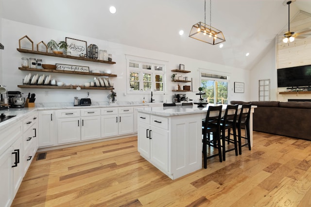 kitchen featuring light wood-type flooring, decorative light fixtures, a center island, and white cabinets