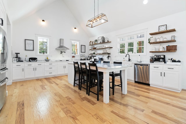 kitchen with wall chimney range hood, white cabinetry, and stainless steel appliances