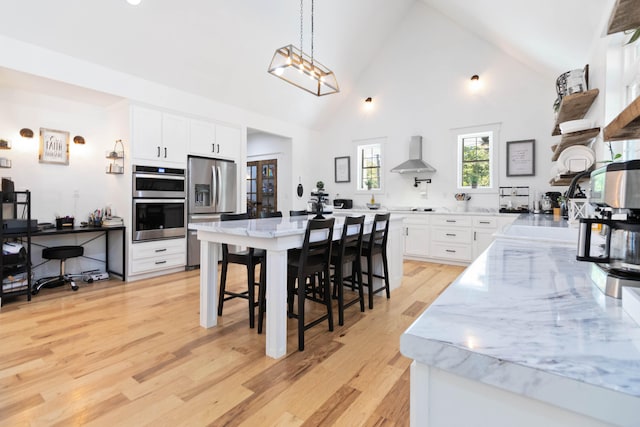 kitchen with wall chimney range hood, a breakfast bar area, stainless steel appliances, high vaulted ceiling, and white cabinetry