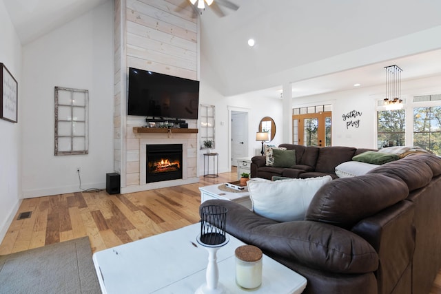 living room with ceiling fan, french doors, high vaulted ceiling, a large fireplace, and hardwood / wood-style floors