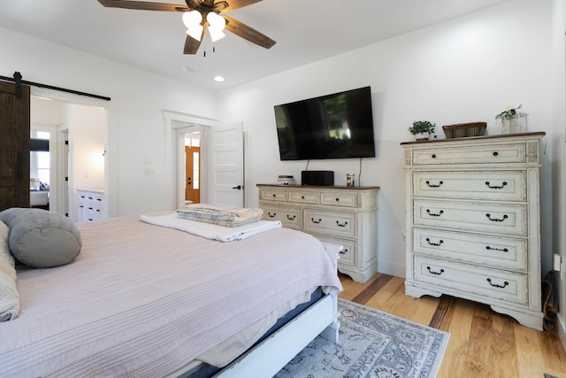 bedroom featuring a barn door, light hardwood / wood-style floors, and ceiling fan