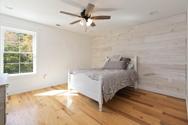 bedroom with wooden walls, ceiling fan, and light hardwood / wood-style flooring