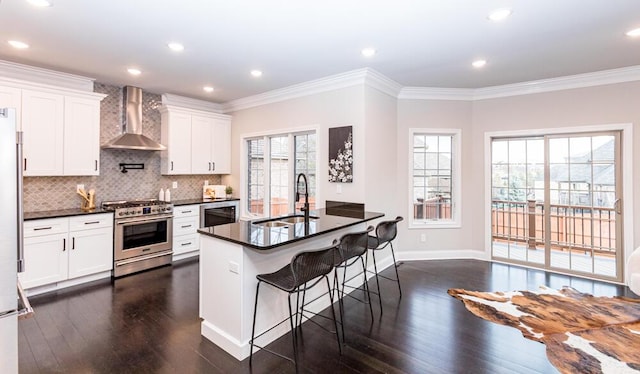 kitchen with stainless steel appliances, dark countertops, a sink, and wall chimney range hood