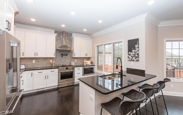 kitchen featuring a breakfast bar area, stainless steel appliances, a sink, wall chimney exhaust hood, and crown molding