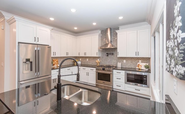 kitchen featuring premium appliances, wall chimney exhaust hood, white cabinetry, a sink, and recessed lighting