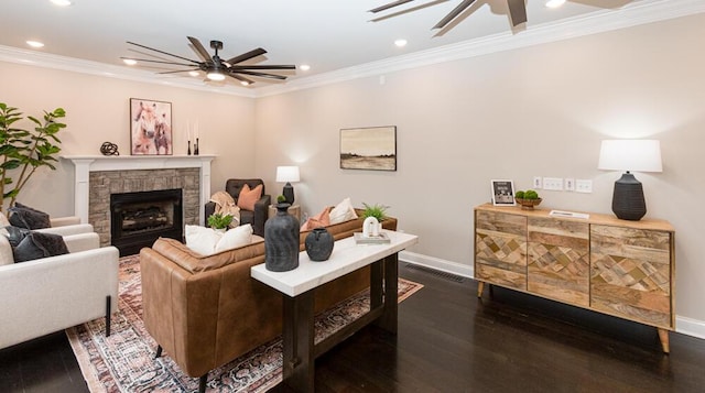 living area featuring visible vents, dark wood finished floors, ceiling fan, crown molding, and a stone fireplace