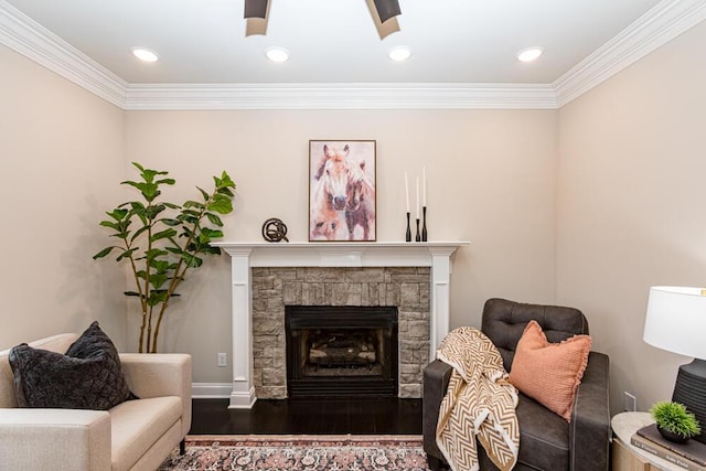 living area with ornamental molding, ceiling fan, a stone fireplace, and wood finished floors