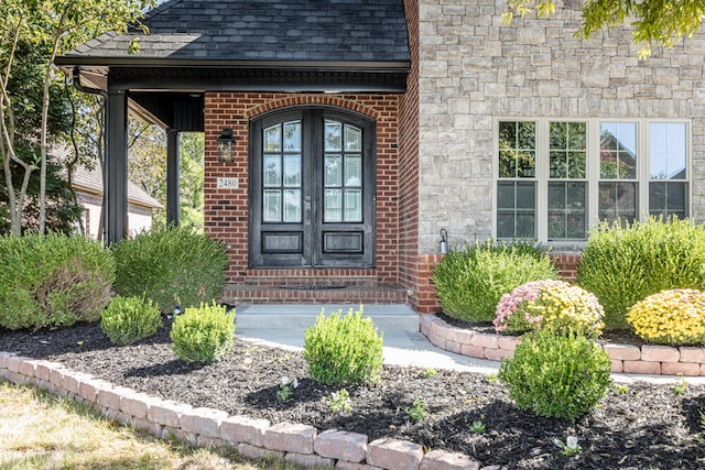 doorway to property with stone siding, roof with shingles, and brick siding