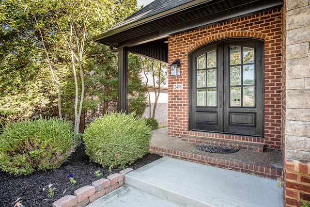 entrance to property featuring french doors, brick siding, and roof with shingles