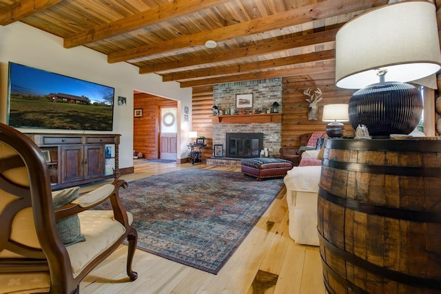 living room featuring beam ceiling, light hardwood / wood-style flooring, wood ceiling, wooden walls, and a fireplace