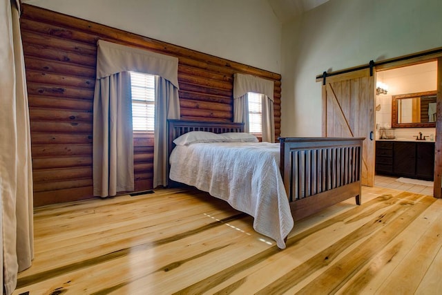 bedroom with light wood-type flooring, ensuite bathroom, a barn door, and log walls