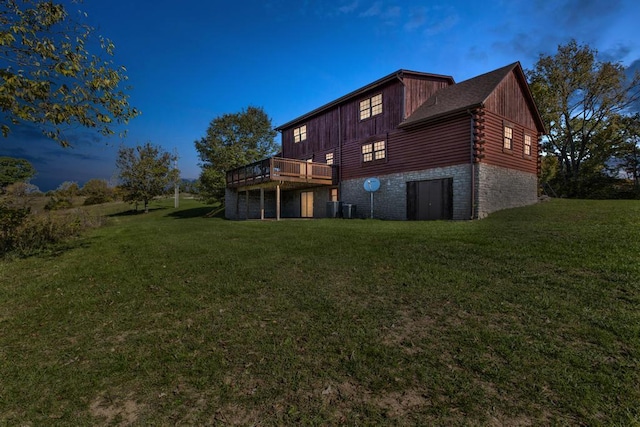 back house at dusk featuring a wooden deck and a yard