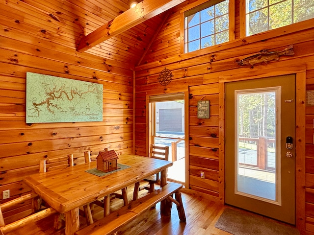 dining space with vaulted ceiling with beams, wood walls, wood ceiling, and light hardwood / wood-style floors