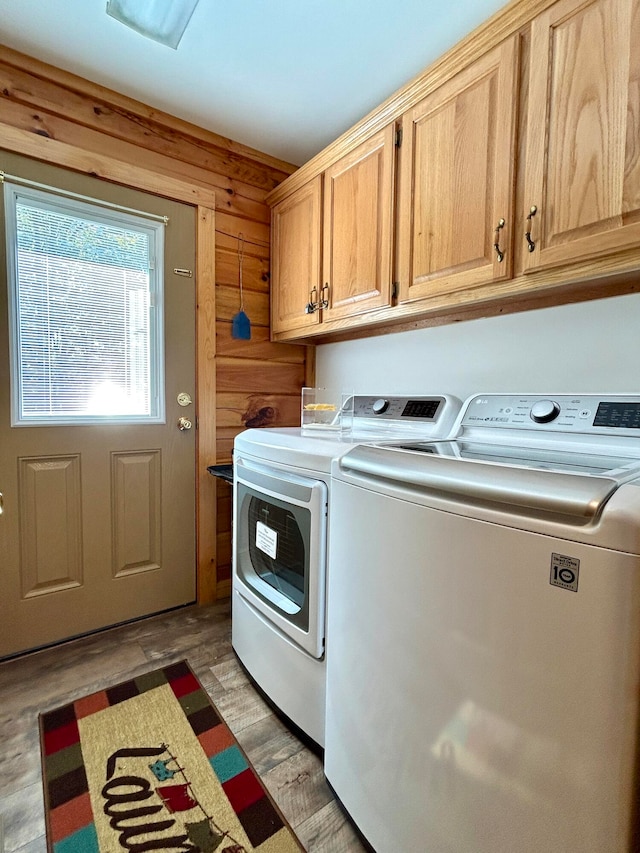 laundry room featuring cabinets, wood walls, light hardwood / wood-style floors, and washing machine and dryer