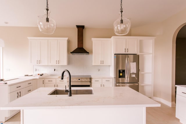 kitchen with sink, hanging light fixtures, wall chimney exhaust hood, an island with sink, and stainless steel fridge with ice dispenser