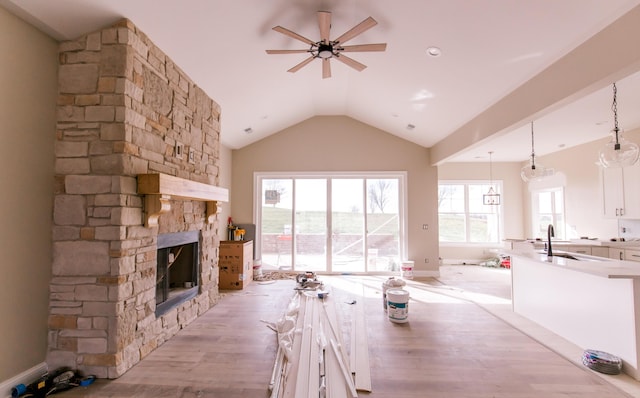 unfurnished dining area with lofted ceiling, a stone fireplace, sink, ceiling fan, and light wood-type flooring