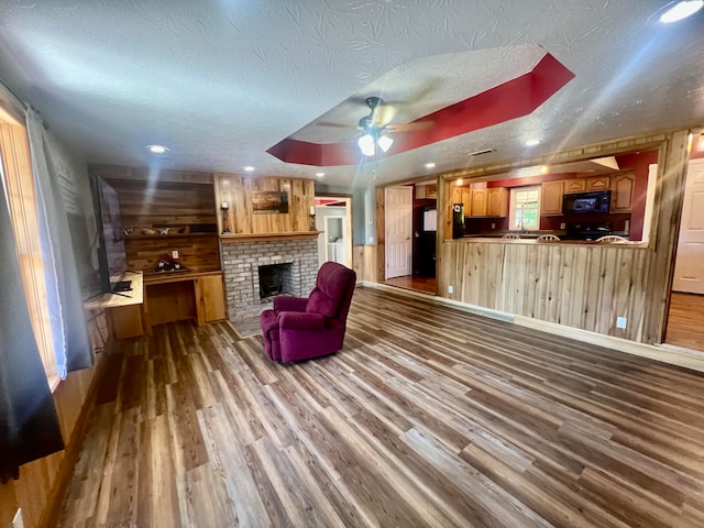 living room with wood-type flooring, ceiling fan, wooden walls, and a textured ceiling