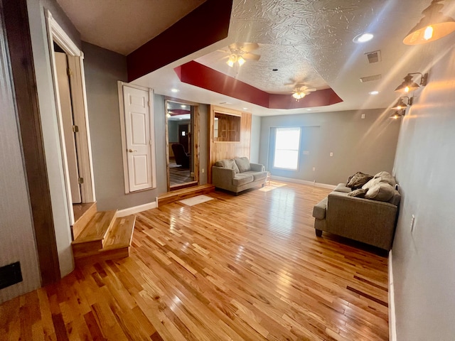 living room featuring a tray ceiling, light hardwood / wood-style flooring, a textured ceiling, and ceiling fan