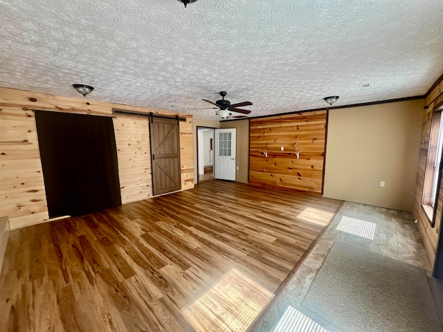 unfurnished living room with a barn door, wood walls, wood-type flooring, and a textured ceiling