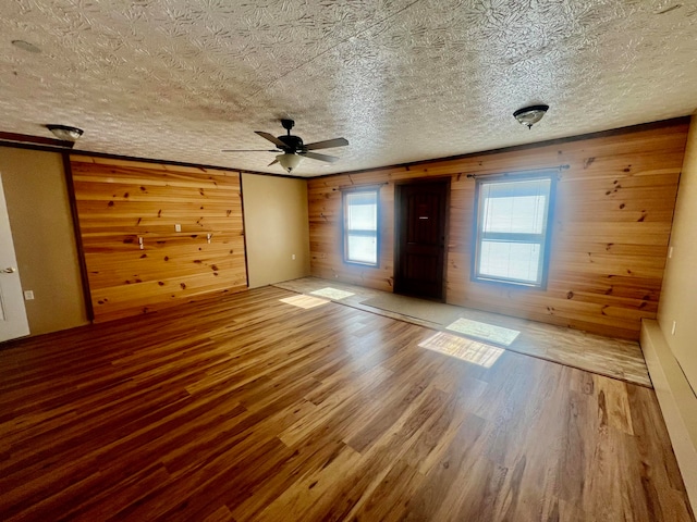 interior space with ceiling fan, wood walls, wood-type flooring, and a textured ceiling