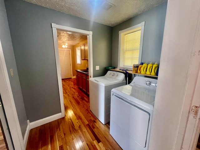 clothes washing area with separate washer and dryer, a textured ceiling, and light wood-type flooring