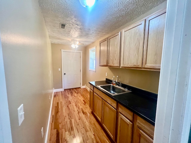 kitchen featuring ceiling fan, sink, light hardwood / wood-style floors, and a textured ceiling