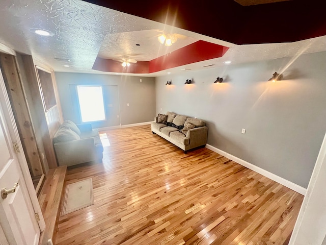 sitting room with a tray ceiling, light hardwood / wood-style flooring, a textured ceiling, and ceiling fan