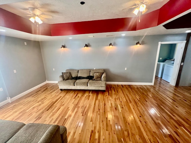 living room with ceiling fan, independent washer and dryer, wood-type flooring, and a textured ceiling